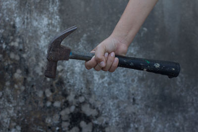 Cropped hand of person holding hammer against wall