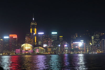 Illuminated buildings by river against sky in city at night