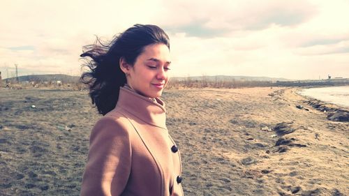 Smiling young woman standing on beach against sky