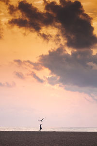 Woman walking at beach against sky during sunset