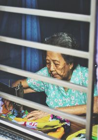 Senior woman sewing on table seen through window