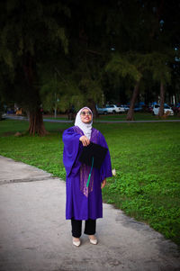Portrait of woman standing on grass against trees