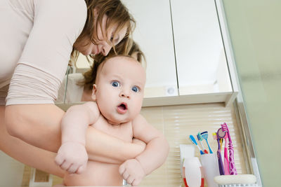 Low angle view of mother carrying shirtless son in bathroom at home