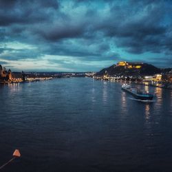 Illuminated city by sea against sky