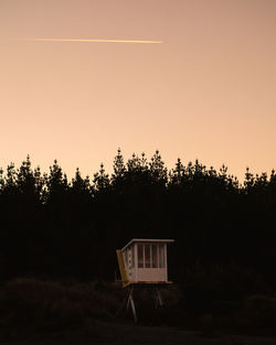 Silhouette house and trees against sky during sunset