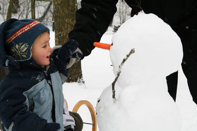 Midsection of parent with boy making snowman during winter