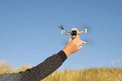 Male hand holding landing drone dji mavic mini against blue sky.