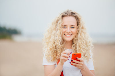 Portrait of smiling young woman using mobile phone at beach