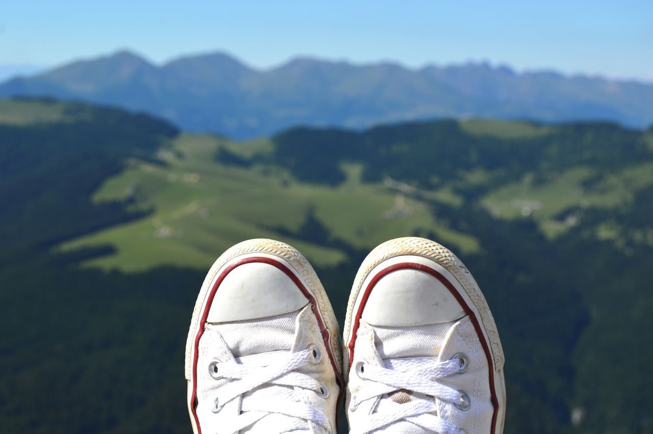 low section, shoe, person, personal perspective, lifestyles, mountain, leisure activity, footwear, human foot, standing, unrecognizable person, landscape, tranquility, part of, sky, nature, mountain range, tranquil scene, outdoors, scenics, day, casual clothing, non-urban scene, beauty in nature, close-up