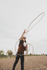 Cowgirl throwing lasso while standing at ranch against sky