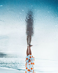 Person hand by sea against sky