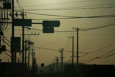 Low angle view of silhouette electricity pylons against sky during sunset