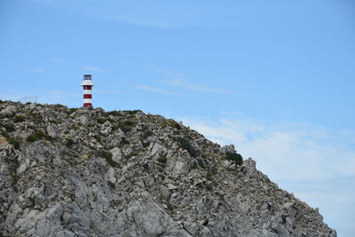 Lighthouse on rock by building against sky