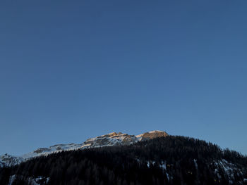 Low angle view of snowcapped mountain against clear blue sky at sunrise 