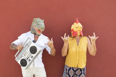 Midsection of people holding mask against orange background