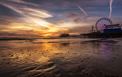 Ferris wheel at beach against sky during sunset