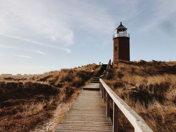 Footpath leading towards lighthouse amidst buildings against sky