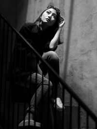 Portrait of young woman sitting on staircase against wall