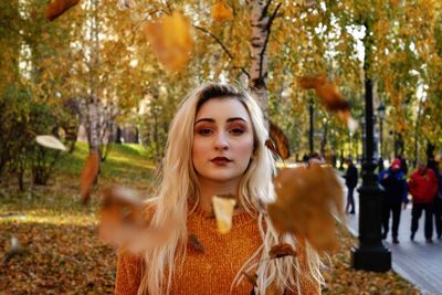 Portrait of beautiful woman standing with falling autumn leaf in park