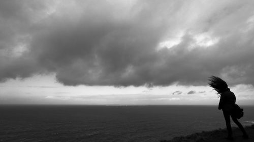 Rear view of silhouette person standing by sea against sky