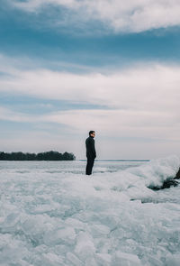 Man standing on an icy shoreline of a lake looking into the distance.