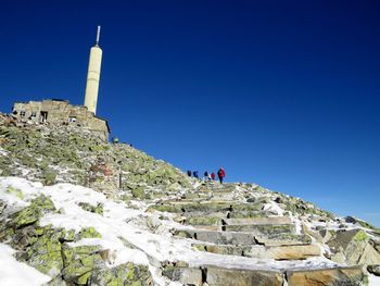 Low angle view of people on mountain against clear blue sky