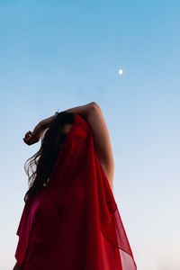 Model covering half of her face with fabric and the moon is visible in the background.