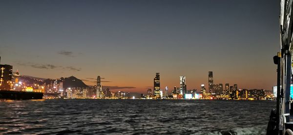 Illuminated buildings by sea against sky at night