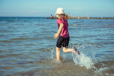Girl running in sea against blue sky
