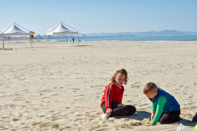 Children playing with sand at beach against clear sky