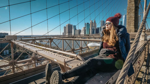 Woman sitting on bridge against cityscape