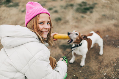 Happy teenage girl hugging and feeding her dog jack russell terrier in a field against the backdrop