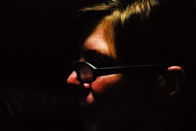 Close-up of woman wearing eyeglasses against black background