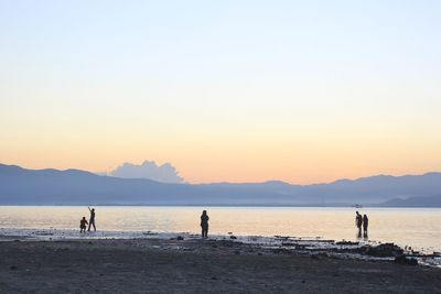 Silhouette people at beach against clear sky during sunset