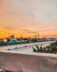 Road by buildings against sky during sunset in city