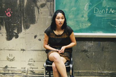 Woman sitting on chair against chalkboard on old wall