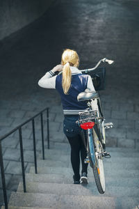 Rear view of businesswoman carrying bicycle while moving down steps