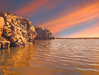 Rocks by sea against sky during sunset