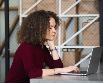 Portrait of a young beautiful serious woman with curly hair working in cafe on laptop.