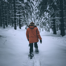 Rear view of man walking on snow covered field in forest