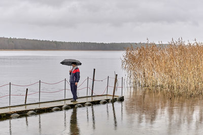 Rear view of woman standing by lake against sky