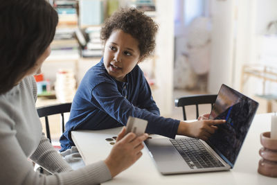 Son pointing at laptop screen while looking at mother holding credit card