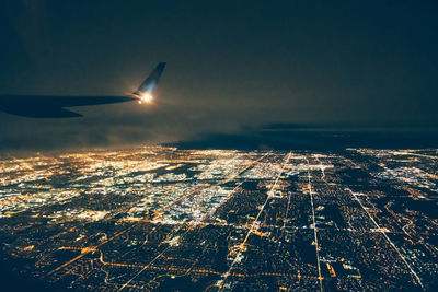 Airplane flying over illuminated cityscape against sky at night