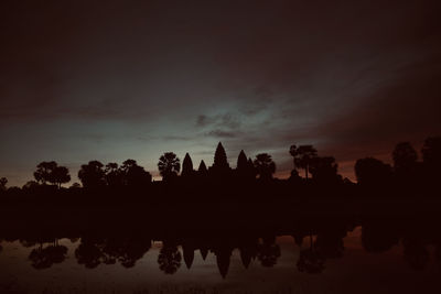 Silhouette trees by lake against sky during sunset