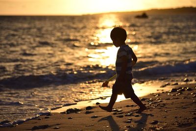 Full length of boy with toy walking on shore at beach during sunset