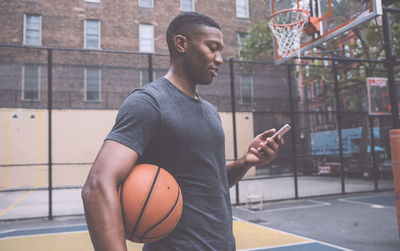 Young man using mobile phone while standing in basketball court