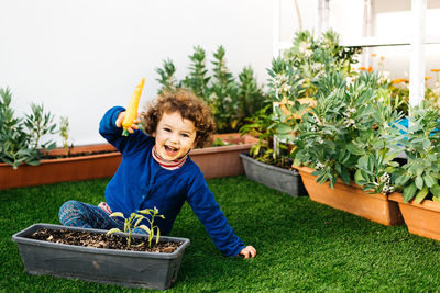 Full length of boy holding toy over flower pot at lawn