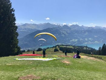 People with parachute on field against mountains in sunny day