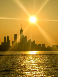 Sea by modern buildings against sky during sunset