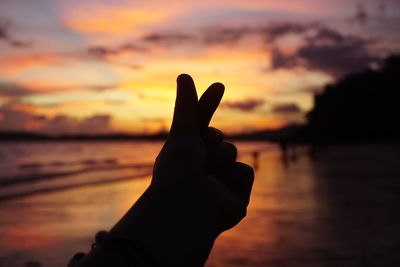 Silhouette of hand gesturing against sky during sunset